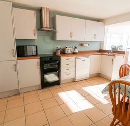 A kitchen with white cabinets black oven white dishwasher wooden dining table and chairs at Malltraeth Cottage in Malltraeth