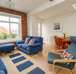 A living room with blue sofas and an armchair a round wooden dining table with chairs and flowers on it at ODYSEA Weymouth
