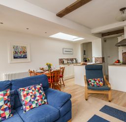 A living area with a blue sofa and chair with colorful cushions a wooden dining table set with dishes a kitchen area with white cabinets and a wooden door at ODYSEA in Weymouth