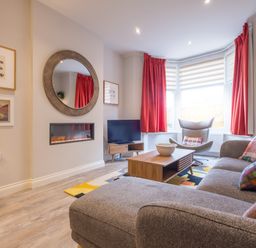 A living room with a gray sofa, wooden coffee table, armchair by a bay window with red curtains at Howe Keld 1 Ground floor Keswick