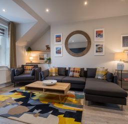 A living room with a dark gray sofa and armchair with plaid cushions and a wooden coffee table on a colorful rug at Howe Keld 4 First floor in Keswick