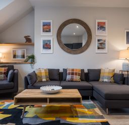A living room with a sectional sofa and armchair a wooden coffee table and a large round mirror on the wall at Howe Keld 4 First floor in Keswick