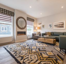 A living room with a patterned rug sofa armchair coffee table and a round mirror at Howe Keld 5 First Floor in Keswick
