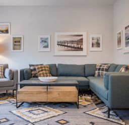 A living room with a gray armchair and sectional sofa a wooden coffee table with a decorative bowl and framed pictures on the walls at Howe Keld 5 First Floor Keswick