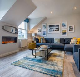 A living room with a fireplace a blue sofa and a glass coffee table at Howe Keld 6 Second Floor in Keswick