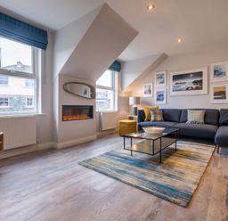 A living room with a sectional sofa, glass coffee table, electric fireplace, and wall art at Howe Keld 6 Second Floor in Keswick