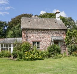 A stone cottage with a garden and flowers in front at Caldhu Cottage in Holmrook