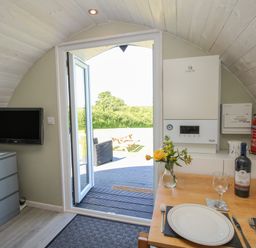 A small dining area with a table set for two a wall-mounted tv and an open door leading outside at Cherry Pod in Hookagate near Meole Brace