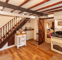 A kitchen with wooden stairs a white oven and an open wooden door leading to a living room at Southcott Farm Cottage in Sheldon