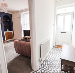 An entryway with patterned tile flooring a wooden bench and coat hooks leading to a living room with a television a sofa and built-in shelves at Aryelle House in Kendal