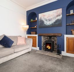 A living room with a gray sofa with pillows a fireplace with a fire and shelves with baskets at Aryelle House in Kendal
