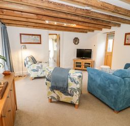 A living room with blue and patterned armchairs a television and wooden beams on the ceiling at The Old Stable in Henryd near Conwy