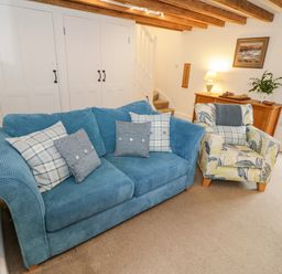 A living room with a blue sofa and a patterned armchair near a wooden cabinet with a lamp and a plant at The Old Stable in Henryd near Conwy