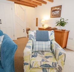 A sitting room with a patterned armchair blue sofa wooden cabinet and staircase at The Old Stable in Henryd near Conwy