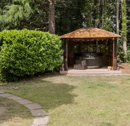 A garden with a path leading to a wooden hot tub gazebo and large bush at The Old Stable in Henryd near Conwy