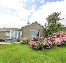 A garden with green grass and pink and purple flowers outside a house at The Headland in Llaneilian near Amlwch