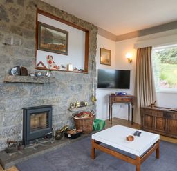 A living room with a stone fireplace wooden coffee table and a large window showing a garden at The Headland in Llaneilian near Amlwch