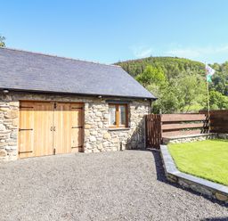 An exterior view of a stone building with wooden double doors next to a small grassy yard and wooden fencing at Glyndwr in Betws-Y-Coed