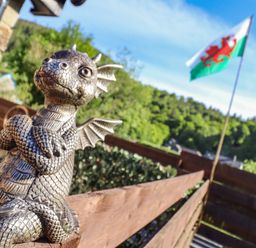 A small dragon statue on a wooden fence with a Welsh flag and trees in the background at Glyndwr in Betws-Y-Coed