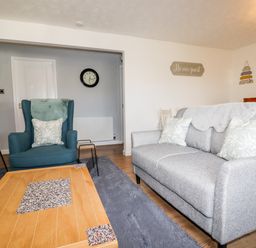 A living room with a blue armchair grey sofa wooden coffee table and a floor lamp at EdyVean Portmellon near Mevagissey