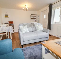 A living room with a grey loveseat two cushions a blue armchair a wooden coffee table and a dining table with chairs at EdyVean in Portmellon near Mevagissey