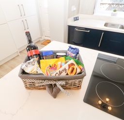 A kitchen countertop with a basket containing a bottle of wine and assorted snacks near a stove and sink at Lobster Pot Retreat in Newbiggin-By-The-Sea