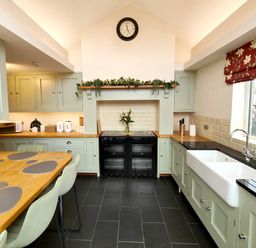 A kitchen with light green cabinets black oven wooden countertops and a dining table at Grove House in Egremont