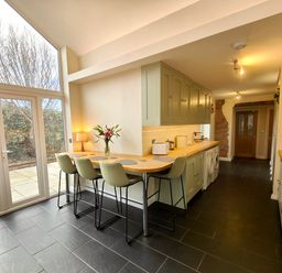 A kitchen with high chairs at a wooden counter and large glass doors at Grove House Egremont