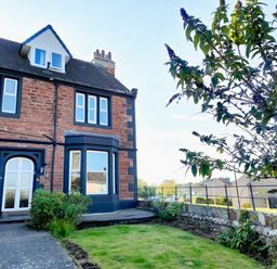 A garden with grass and plants next to a brick house with multiple windows at Grove House in Egremont