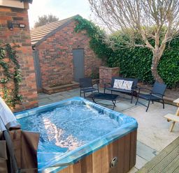 An outdoor patio area with a hot tub black metal chairs a black metal table a wooden picnic table a tree and a brick shed at Grove House in Egremont