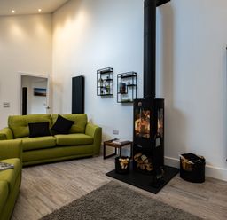 A living room with green sofas a wood burning stove and black radiators at Lowenda in Polzeath