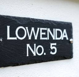 A black slate house nameplate with white text reading Lowenda No 5 on a white wall at Lowenda Polzeath
