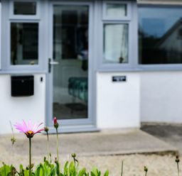 A flower in front of a grey door and white wall with a window at Lowenda in Polzeath