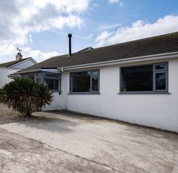 The exterior of a single-story house with white walls gray windows a concrete driveway and a bush in front at Lowenda in Polzeath