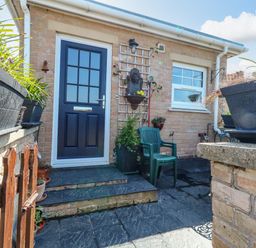 An outdoor patio area with a black door, green plastic chair, potted plants, and brick walls at Beach Retreat in Weymouth