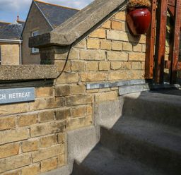 A brick wall with a sign that says Beach Retreat and concrete steps leading up to a wooden gate at Beach Retreat in Weymouth