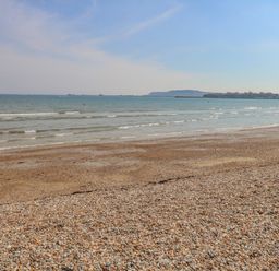 A pebble and sandy beach with small waves and distant land on the horizon at Beach Retreat in Weymouth