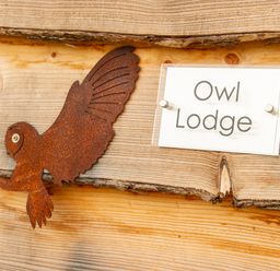 A wooden wall with a metal owl decoration and a sign reading Owl Lodge at Owl Lodge in Wedmore