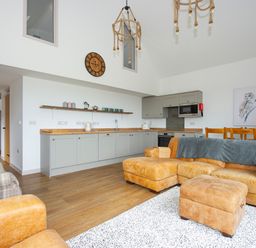 An open plan living room and kitchen with tan leather sofa and ottoman wooden dining chairs and gray kitchen cabinets at Owl Lodge in Wedmore