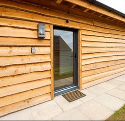 A wooden exterior wall with a glass door and two wall lights at Starling Lodge in Wedmore