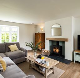 A living room with a grey sofa, wooden coffee table, fireplace with fire, TV, and wooden cabinet at Samphire Rock