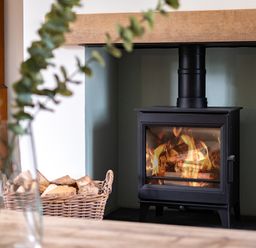 A wood burning stove with fire inside and a basket of firewood beside it at Samphire in Rock