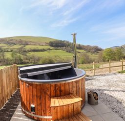 An outdoor wooden hot tub with steps and a chimney on a patio with a fence and hills in the background at Nant y Garnedd Mallwyd near Dinas Mawddwy