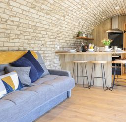 A living area with a gray sofa and pillows next to a kitchen island with wooden stools and a brick arched ceiling at Nant y Garnedd Mallwyd near Dinas Mawddwy