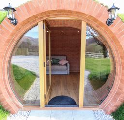 A circular entrance with glass doors leading to a room with a sofa and two cushions at Nant yr Esgair in Mallwyd near Dinas Mawddwy
