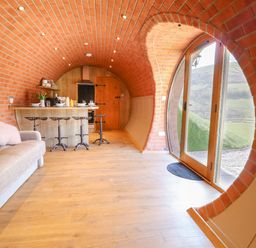 An arched brick interior with a kitchen island and stools a sofa and glass doors opening to outside at Nant yr Esgair Mallwyd near Dinas Mawddwy