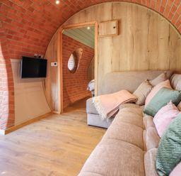 A living space with curved brick walls a wooden door a mounted flat screen tv and a beige sofa with pillows and a throw at Nant yr Esgair Mallwyd near Dinas Mawddwy