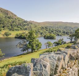 A lake surrounded by hills and trees with a stone wall in the foreground at Kirkstone Lodge in Limefitt Park near Windermere