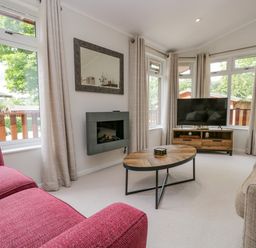 A living room with a red sofa a beige sofa wooden coffee table a wall-mounted fireplace and a television on a wooden stand at Kirkstone Lodge in Limefitt Park near Windermere