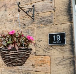 A hanging basket with pink flowers on a stone wall next to a house number sign reading 19 Duke Street at 19 Duke Street in Alnwick